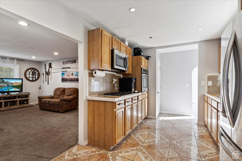 Kitchen with appliances with stainless steel finishes, light colored carpet, tile counters, and tasteful backsplash