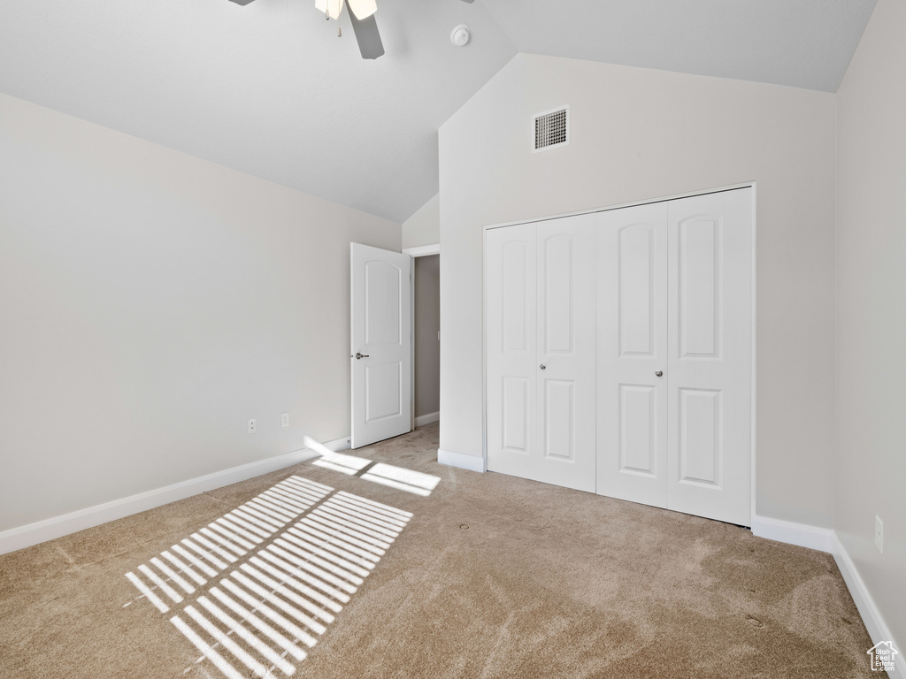 Unfurnished bedroom featuring lofted ceiling, light carpet, a closet, and ceiling fan