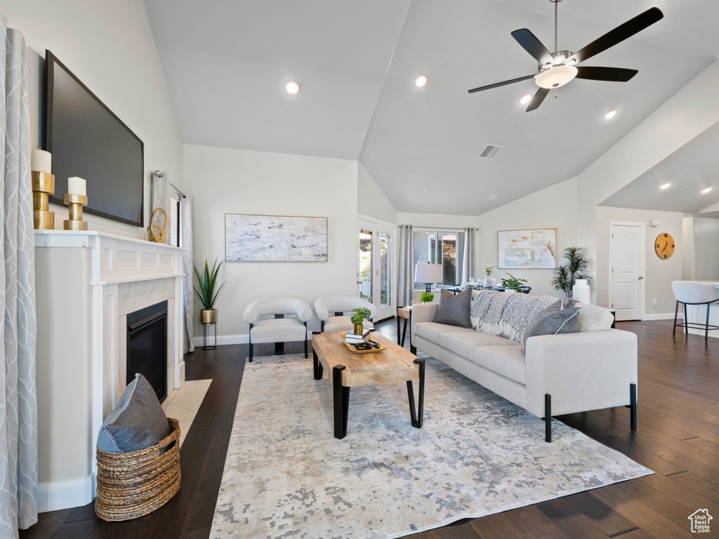 Living room featuring high vaulted ceiling, dark wood-type flooring, a tile fireplace, and ceiling fan