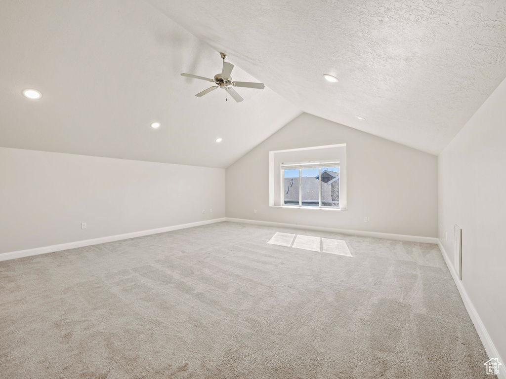 Bonus room with light carpet, a textured ceiling, vaulted ceiling, and ceiling fan