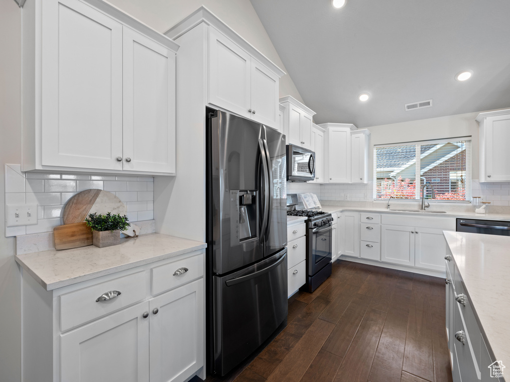 Kitchen with white cabinets, vaulted ceiling, dark hardwood / wood-style floors, sink, and stainless steel appliances