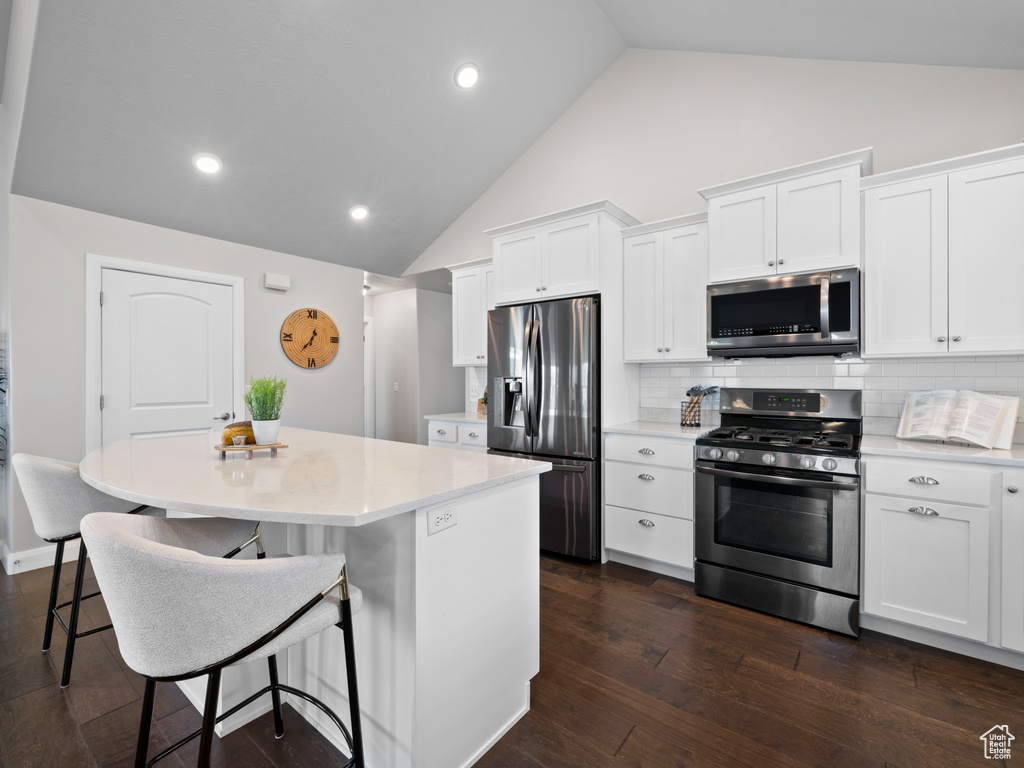 Kitchen featuring a kitchen island, backsplash, stainless steel appliances, white cabinets, and dark hardwood / wood-style floors