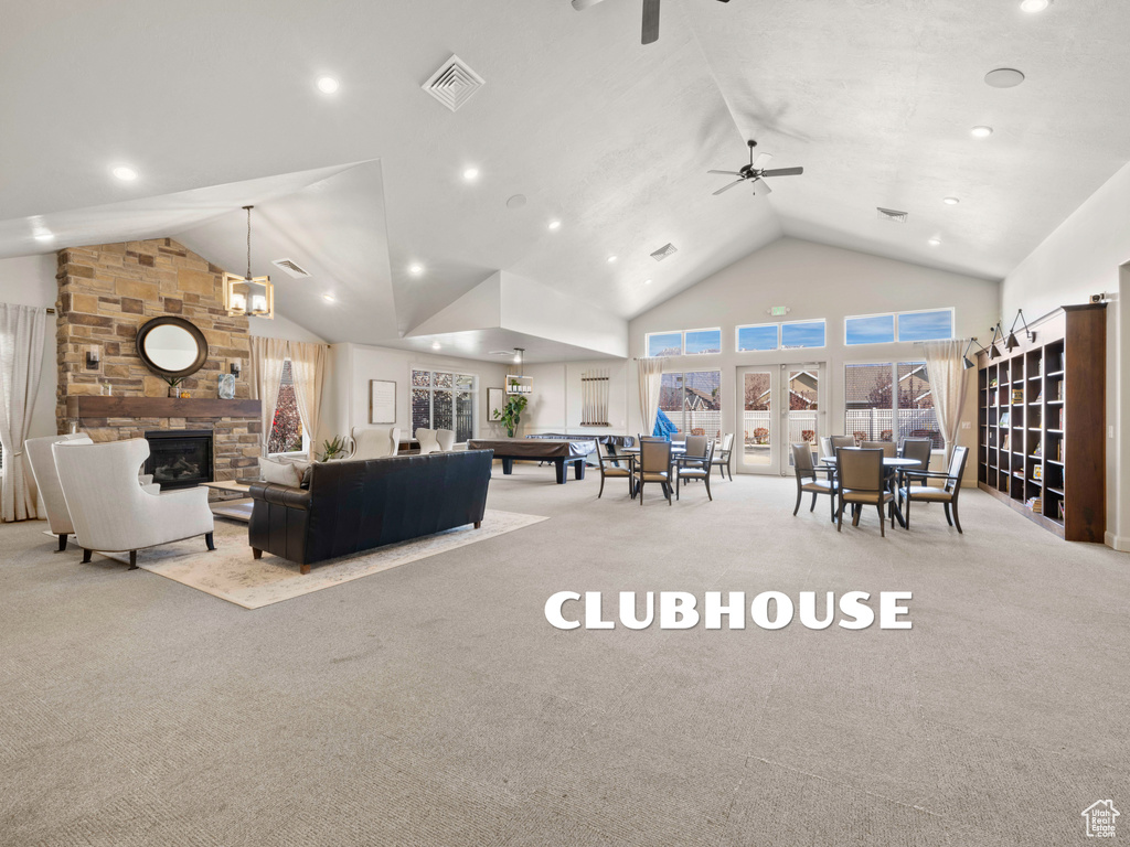 Carpeted living room featuring a stone fireplace, high vaulted ceiling, and ceiling fan