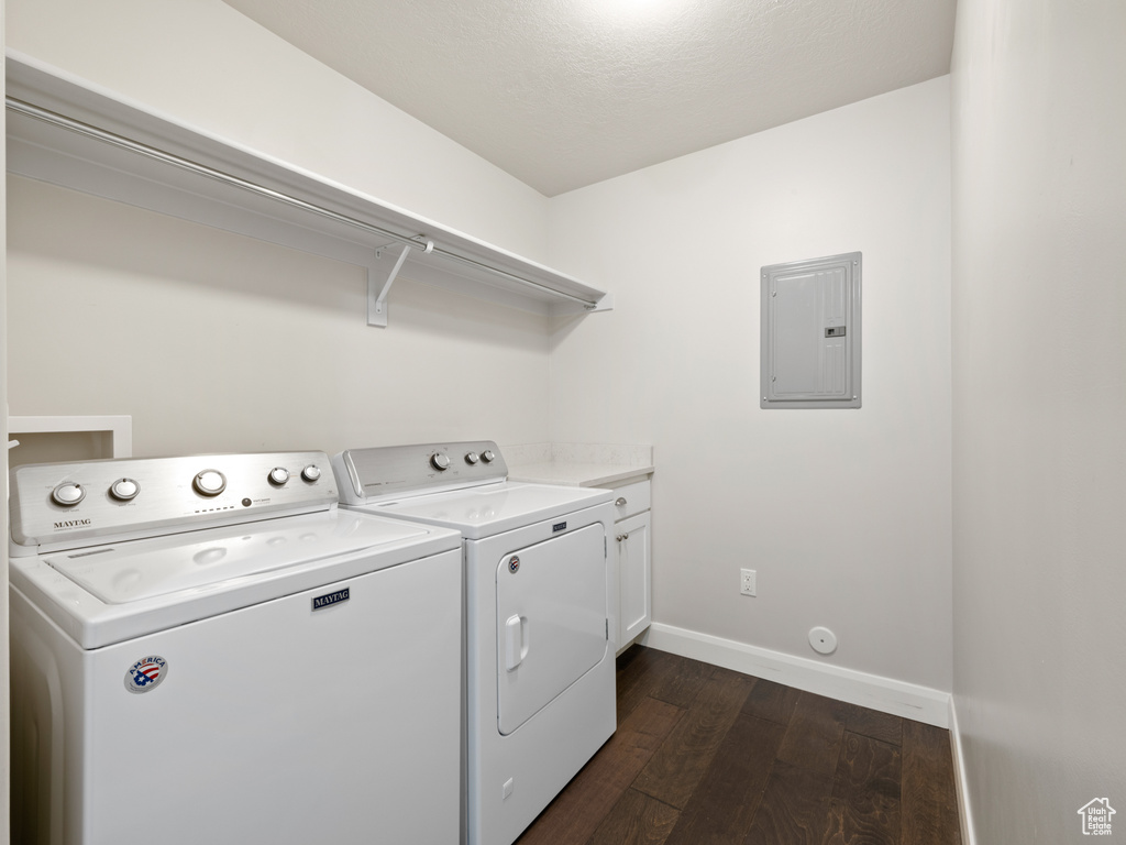 Laundry area with a textured ceiling, electric panel, washer and clothes dryer, dark wood-type flooring, and cabinets