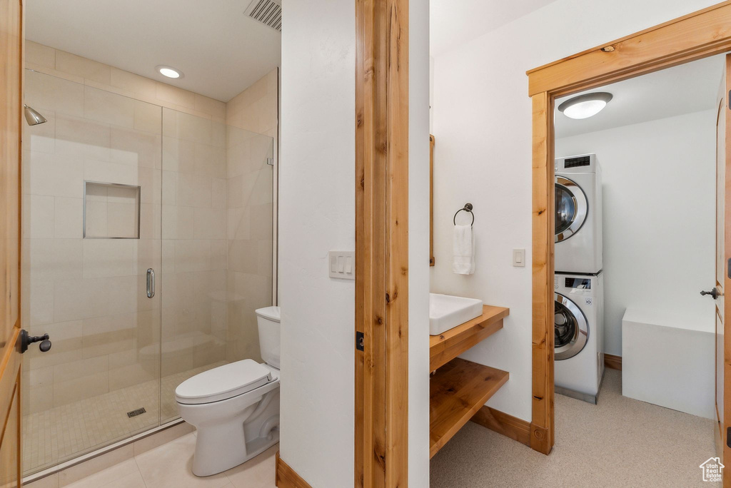 Bathroom with an enclosed shower, toilet, and stacked washing maching and dryer