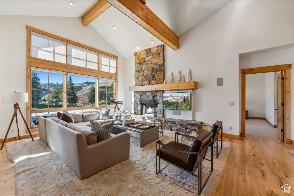 Living room featuring light hardwood / wood-style floors, a stone fireplace, high vaulted ceiling, and beamed ceiling