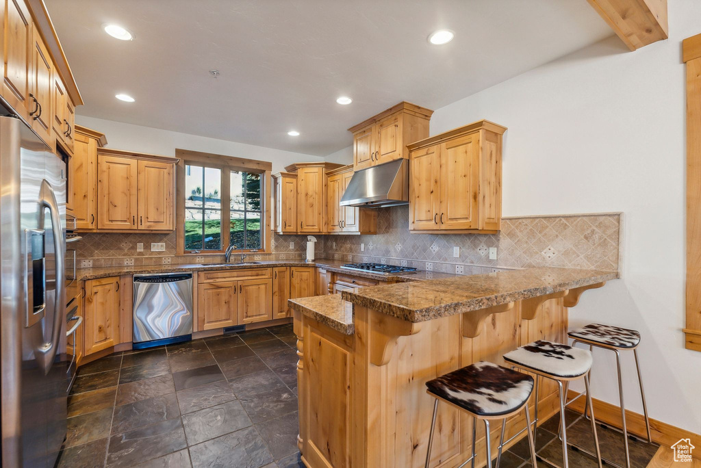 Kitchen featuring appliances with stainless steel finishes, sink, a kitchen bar, kitchen peninsula, and extractor fan