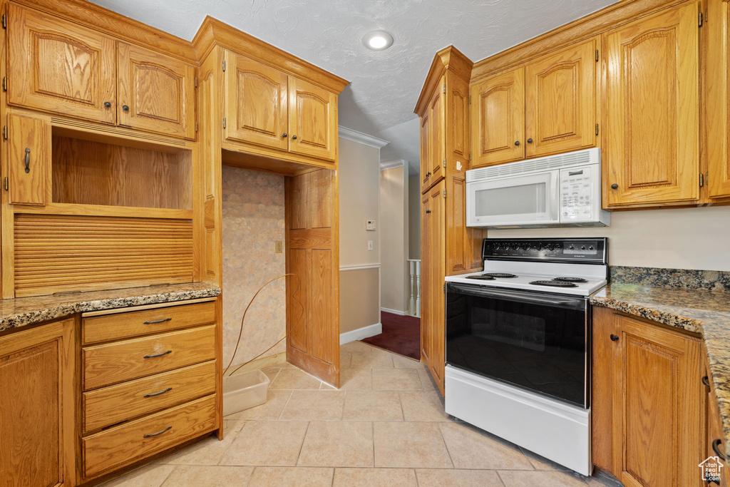 Kitchen with white appliances, light stone countertops, light tile patterned floors, and ornamental molding