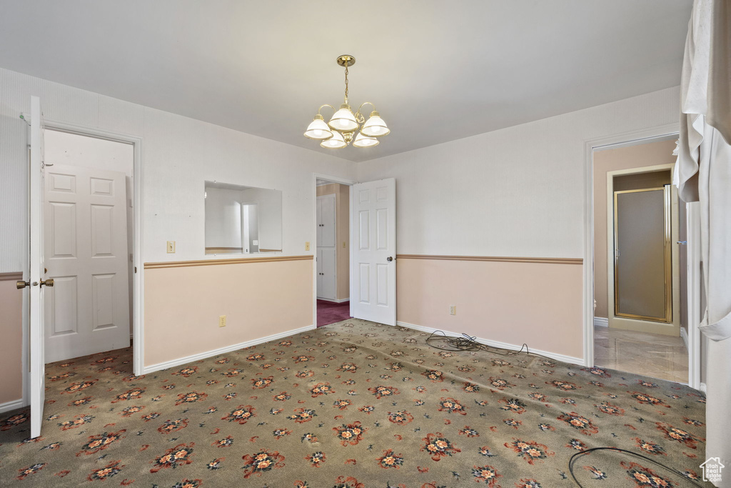 Spare room featuring an inviting chandelier and dark carpet