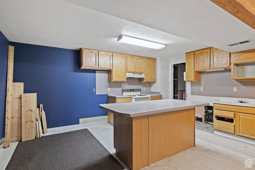 Kitchen with light brown cabinetry, a kitchen island, a textured ceiling, and electric stove