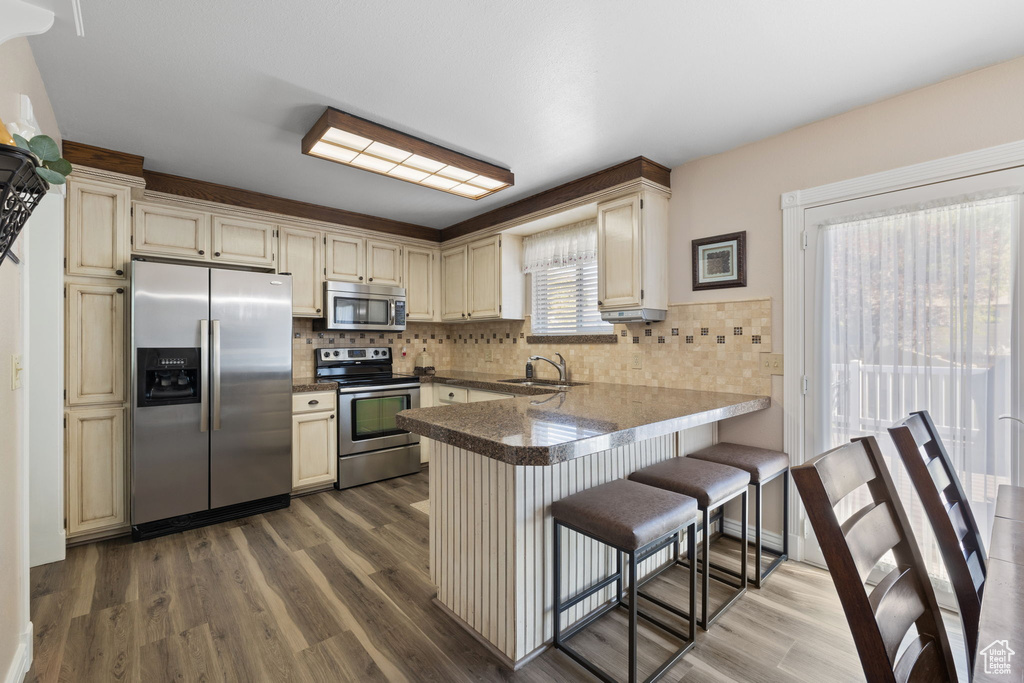 Kitchen with cream cabinets, backsplash, kitchen peninsula, hardwood / wood-style floors, and stainless steel appliances