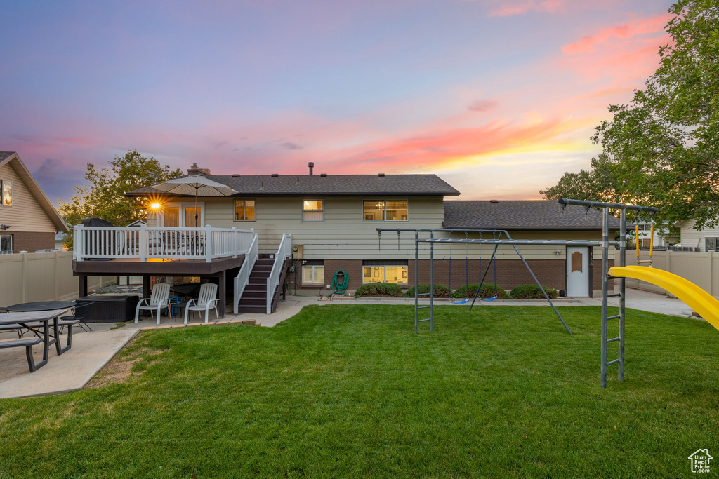 Back house at dusk with a patio, a wooden deck, and a yard