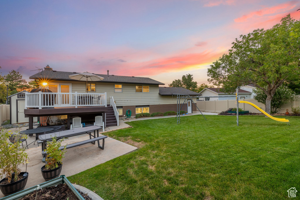 Yard at dusk with a wooden deck, a patio area, and a playground