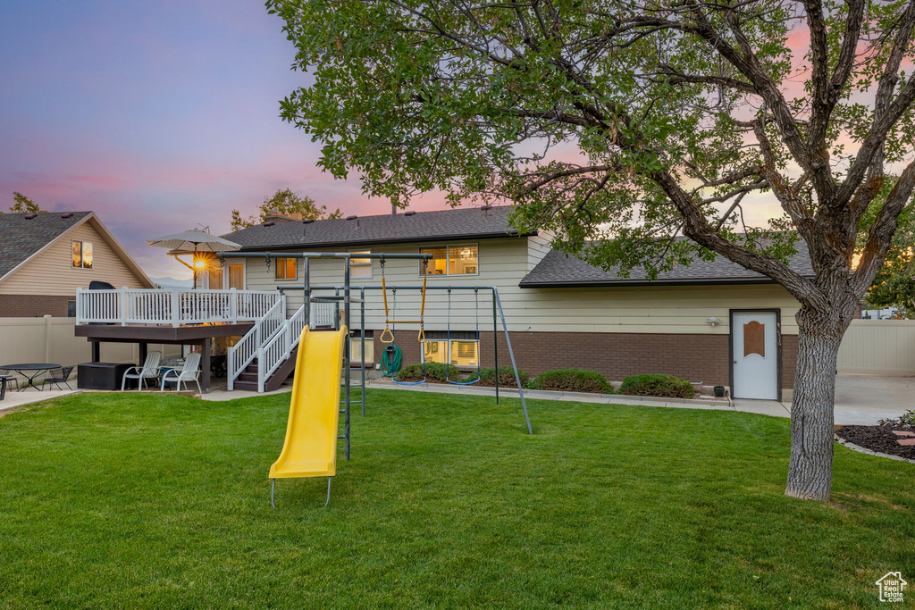 View of front facade with a wooden deck, a patio, a lawn, and a playground