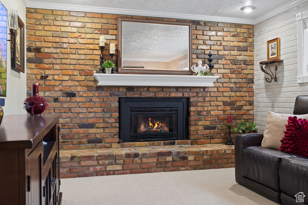 Carpeted living room featuring ornamental molding, a textured ceiling, and a brick fireplace