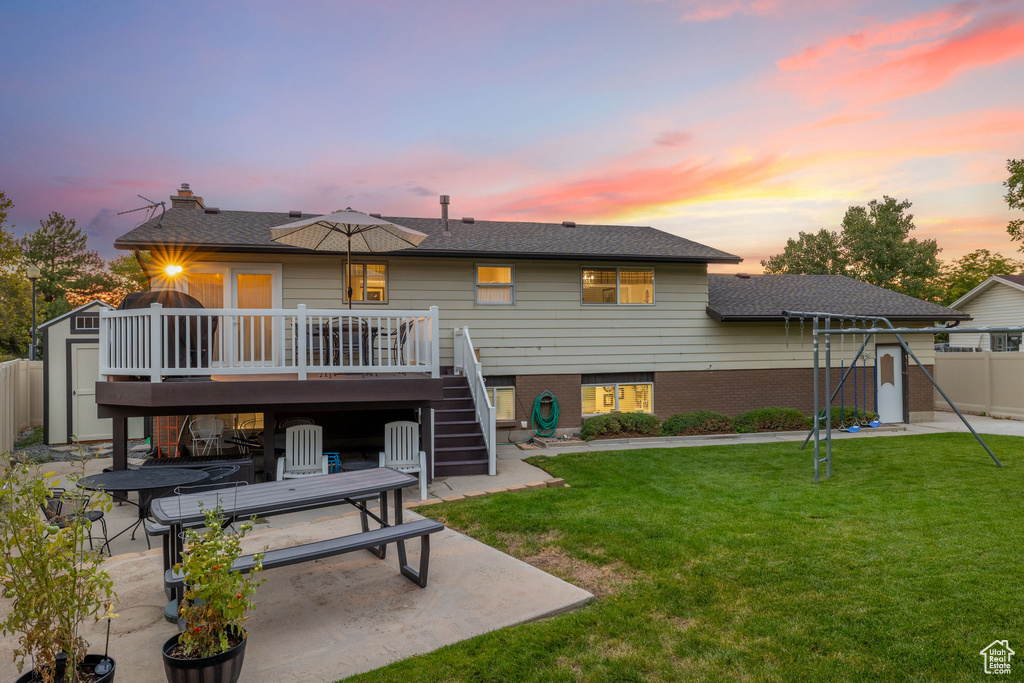 Back house at dusk with a patio area, a deck, and a lawn