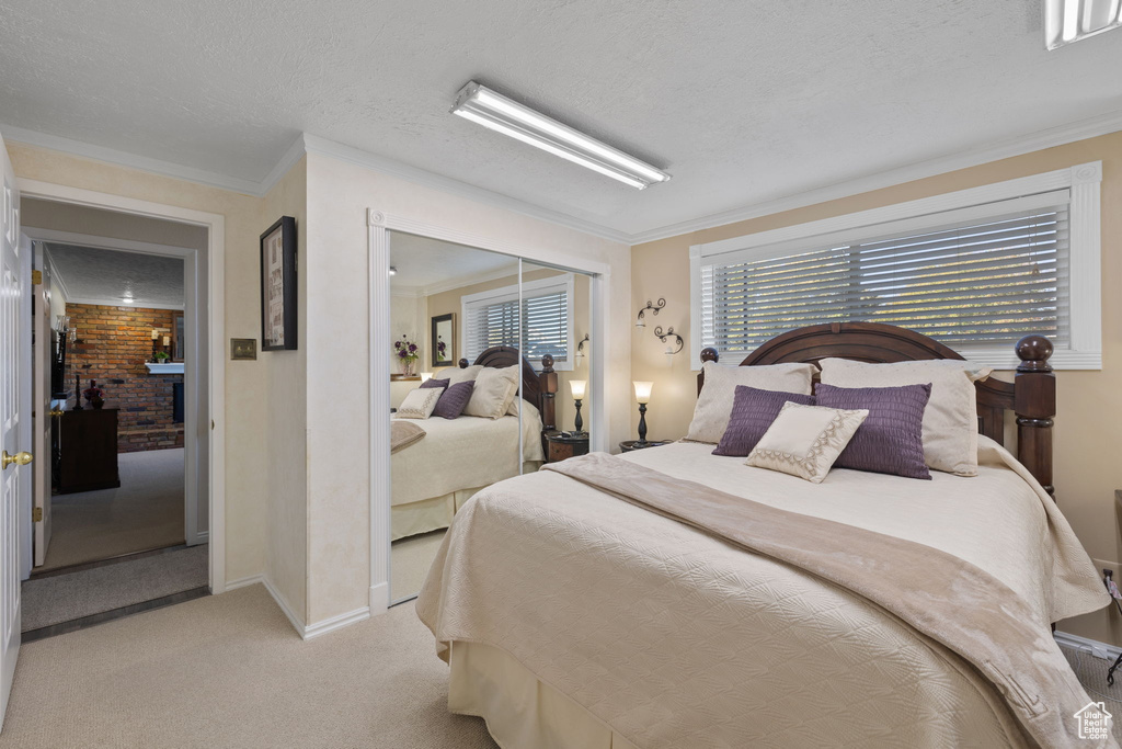 Bedroom with a closet, a textured ceiling, light colored carpet, and crown molding