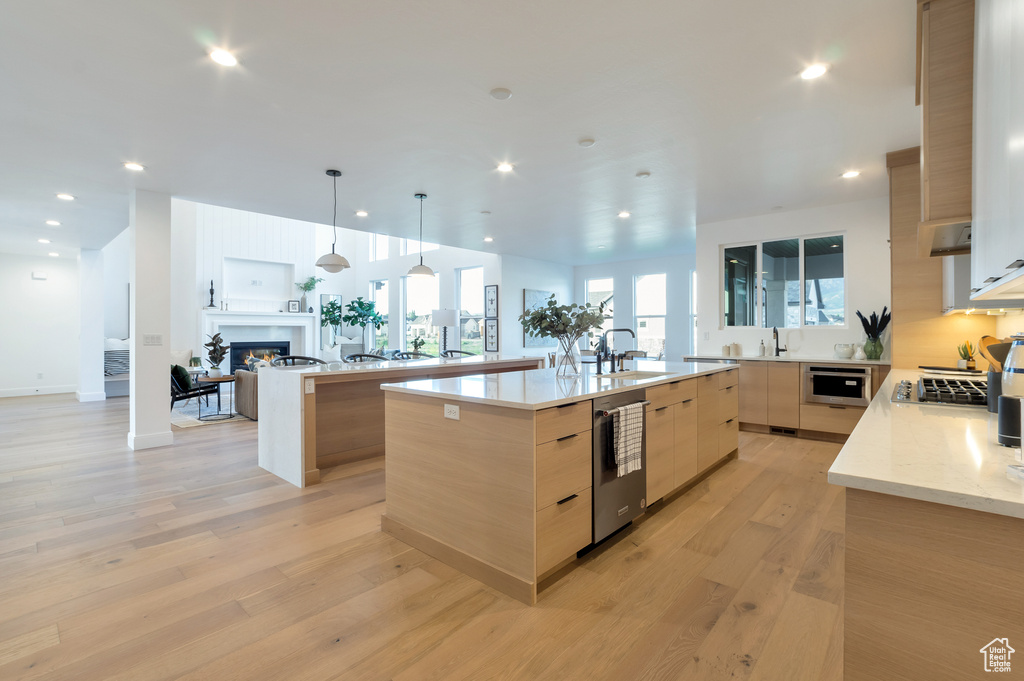 Kitchen with a spacious island, sink, light wood-type flooring, and hanging light fixtures