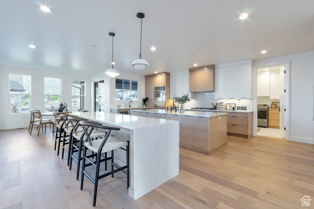 Kitchen featuring a large island with sink, hanging light fixtures, a kitchen bar, light wood-type flooring, and white cabinets