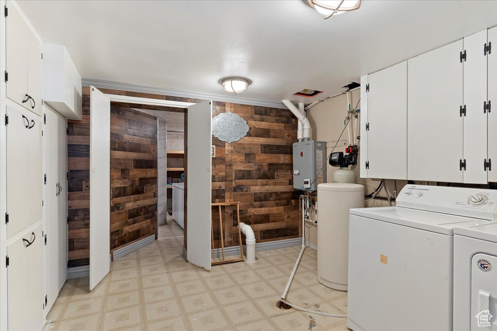 Laundry room with wooden walls, water heater, washing machine and clothes dryer, and cabinets