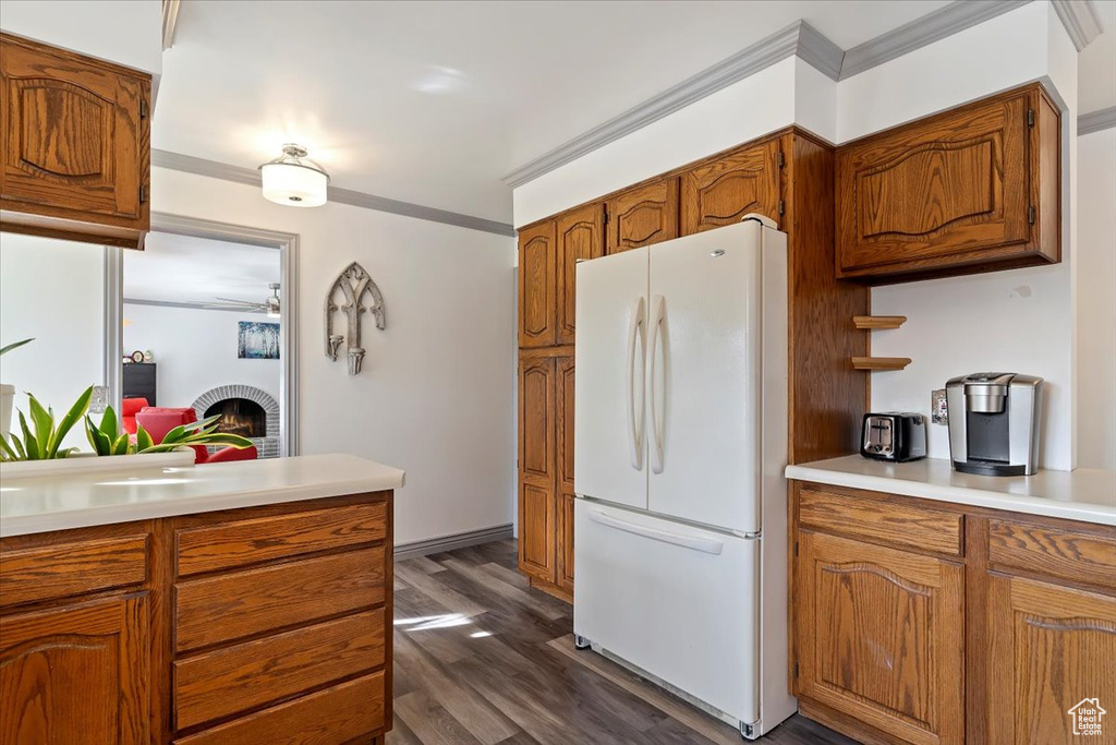 Kitchen featuring dark wood-type flooring, white fridge, crown molding, and a brick fireplace