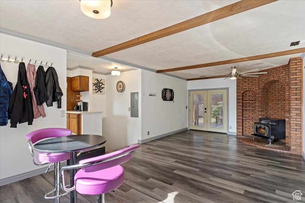 Dining space with beam ceiling, electric panel, a textured ceiling, dark hardwood / wood-style floors, and a wood stove