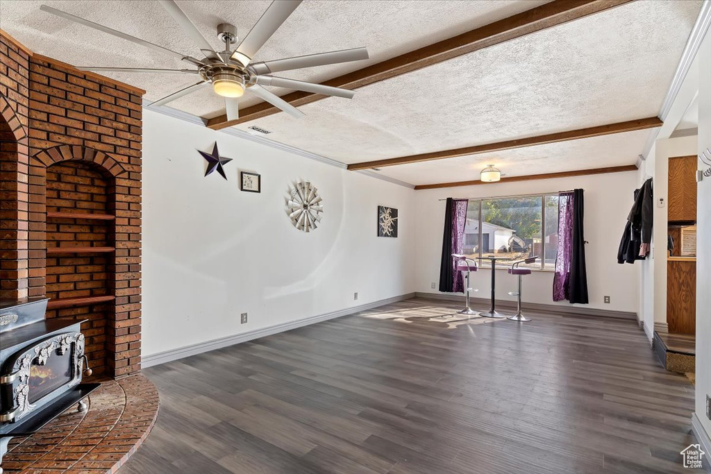 Unfurnished living room featuring a textured ceiling, ceiling fan, dark wood-type flooring, beam ceiling, and ornamental molding