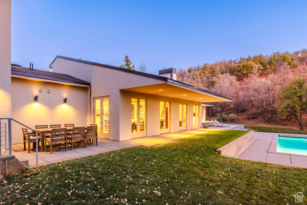 Back house at dusk featuring a yard and a patio area