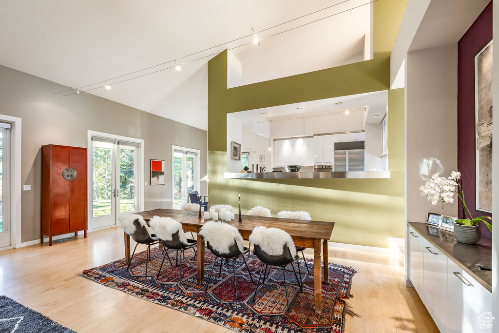 Dining space featuring high vaulted ceiling, rail lighting, and light hardwood / wood-style flooring