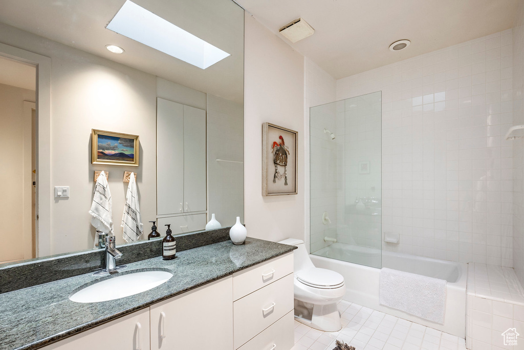 Full bathroom with tiled shower / bath, a skylight, vanity, tile patterned floors, and toilet