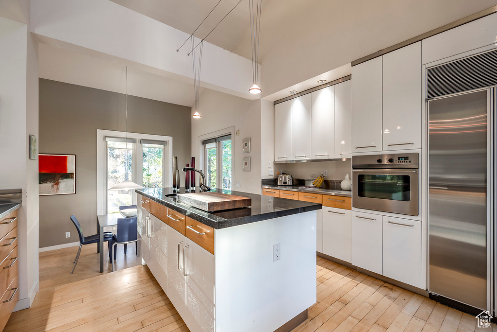 Kitchen with light hardwood / wood-style flooring, white cabinetry, an island with sink, and stainless steel appliances