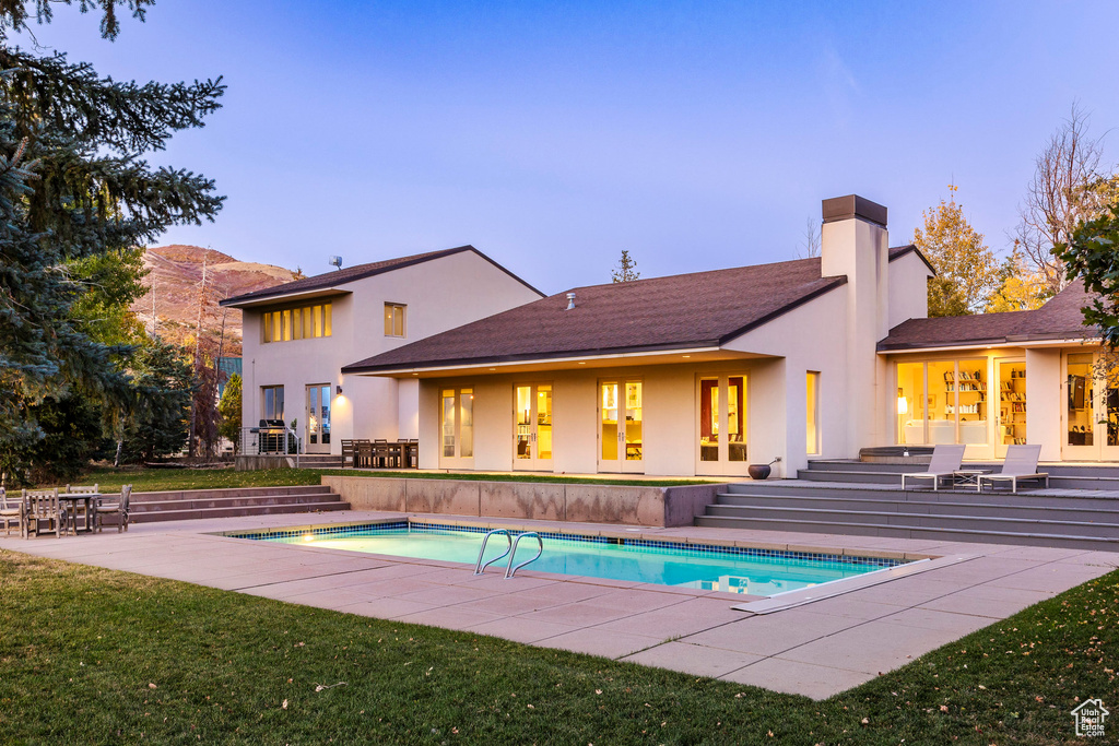 Back house at dusk featuring a mountain view, a yard, french doors, and a patio area