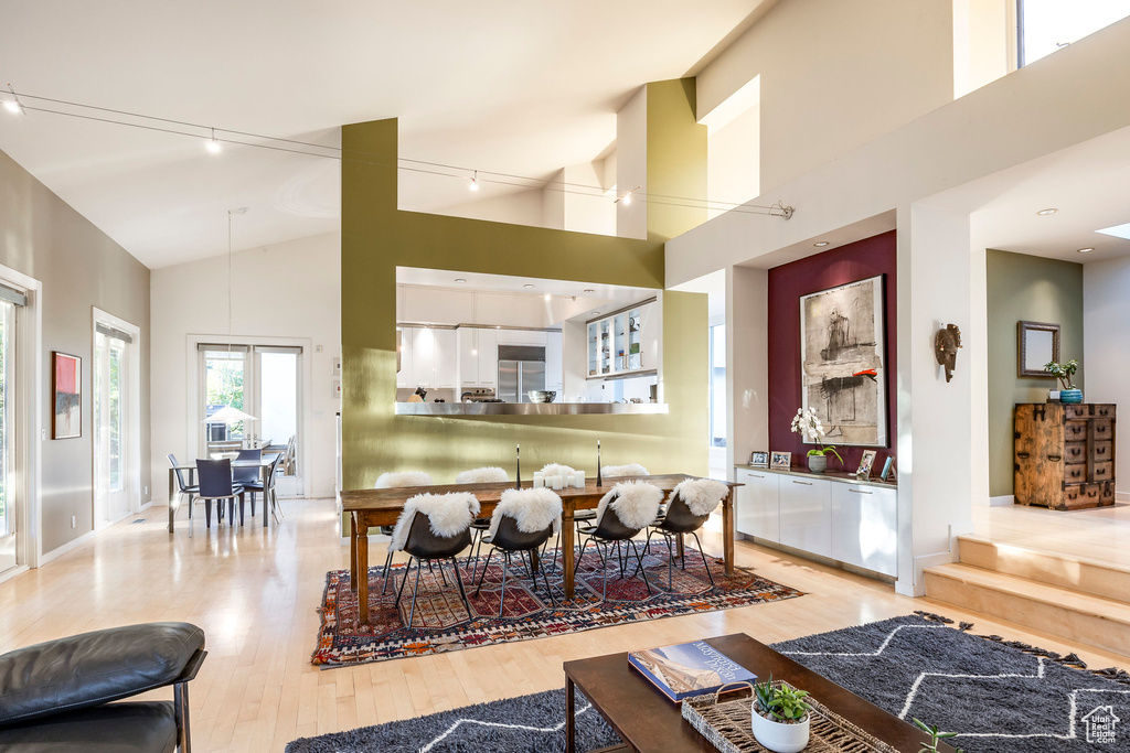 Dining area featuring high vaulted ceiling, rail lighting, and light hardwood / wood-style flooring