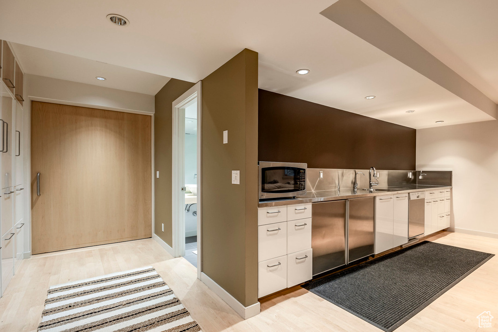 Kitchen featuring stainless steel counters, appliances with stainless steel finishes, sink, white cabinets, and light hardwood / wood-style flooring