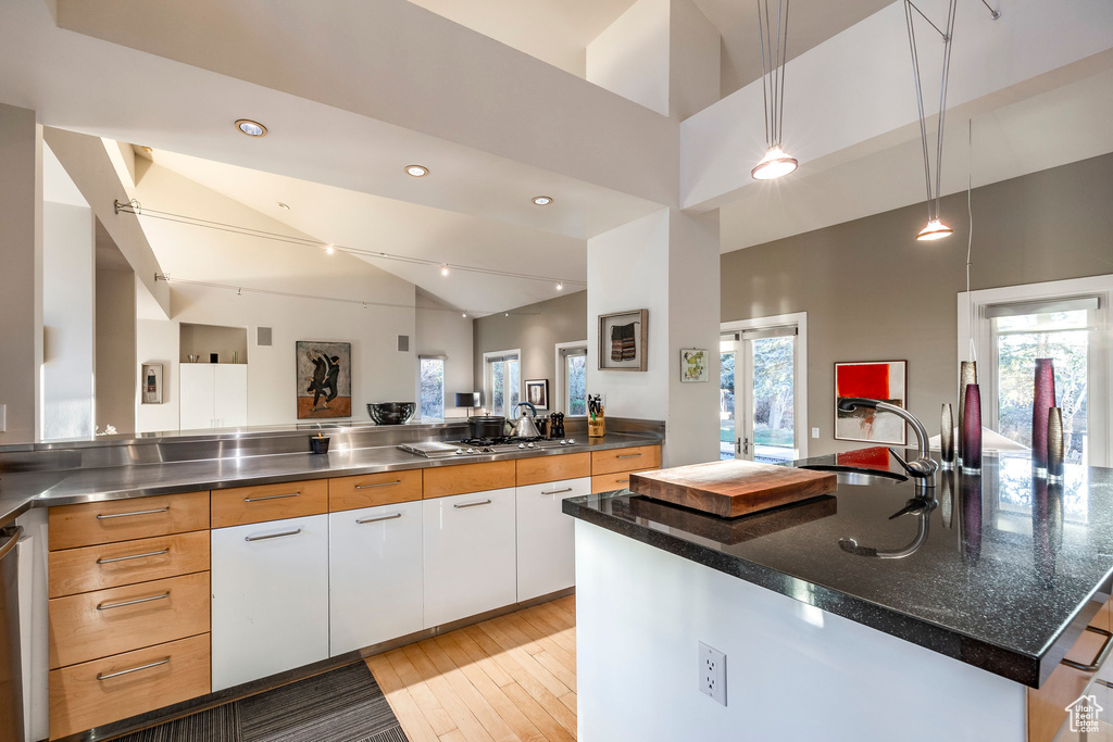 Kitchen with white cabinetry, pendant lighting, sink, light hardwood / wood-style floors, and a kitchen island with sink