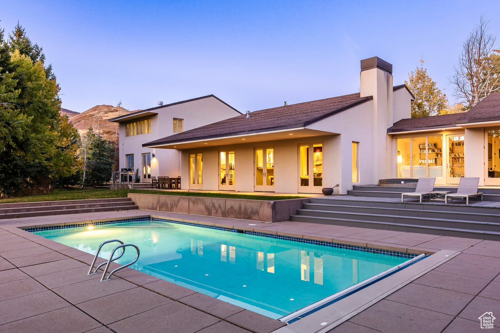 Pool at dusk with a patio, french doors, and a mountain view