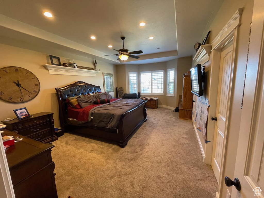 Bedroom featuring light carpet, a raised ceiling, and ceiling fan