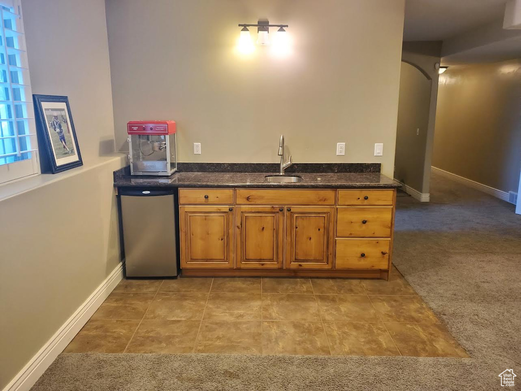 Kitchen with light colored carpet, stainless steel dishwasher, sink, and dark stone counters