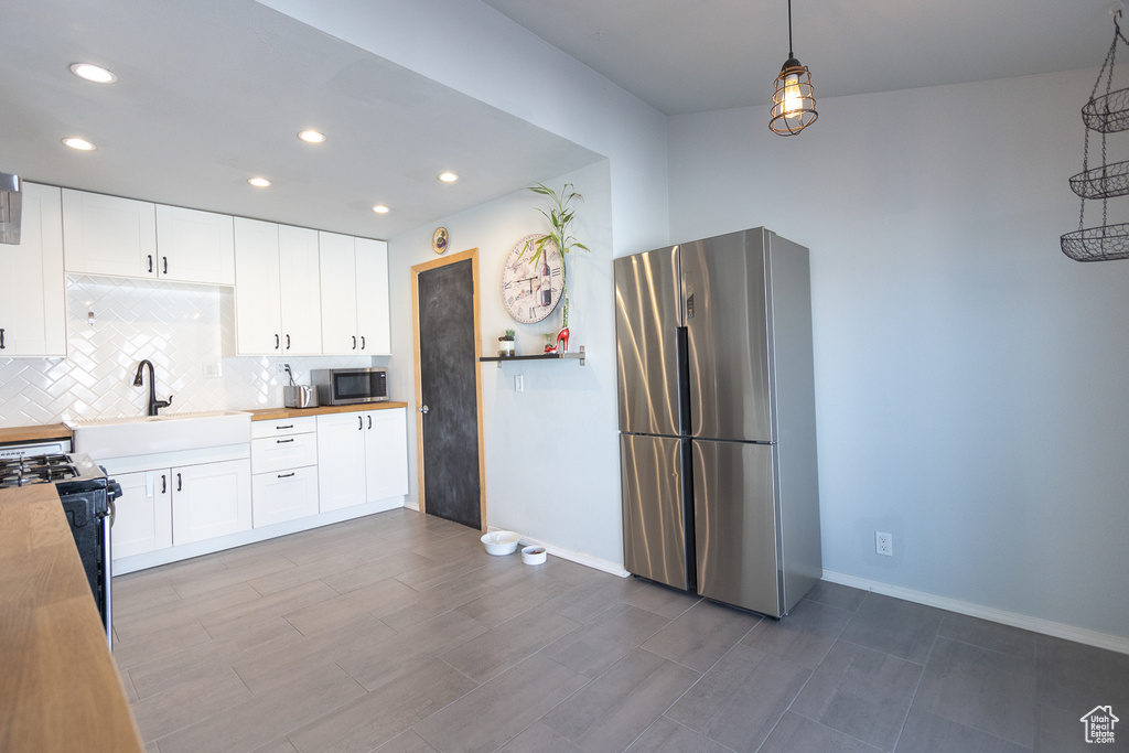 Kitchen with appliances with stainless steel finishes, sink, butcher block counters, pendant lighting, and white cabinets