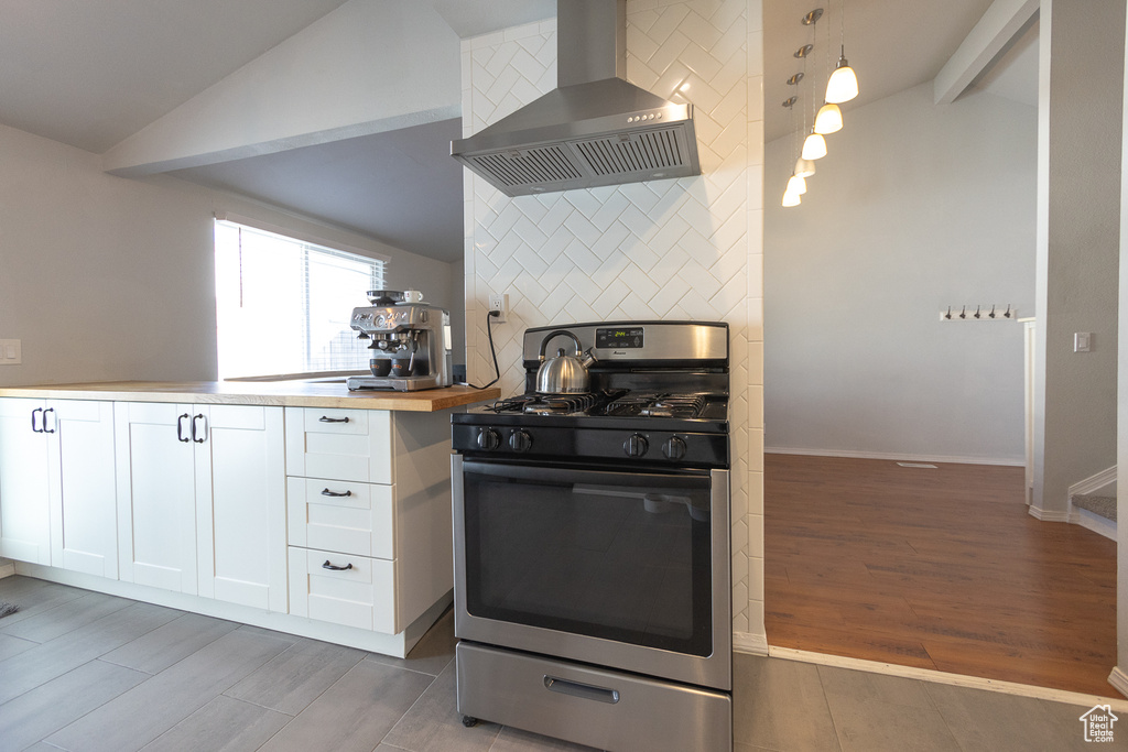 Kitchen featuring stainless steel gas range oven, white cabinetry, vaulted ceiling, light hardwood / wood-style floors, and wall chimney exhaust hood