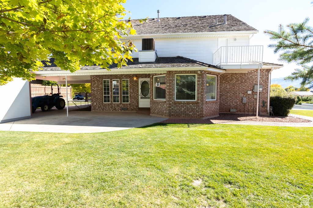 Rear view of house with a balcony, a yard, a patio, and a carport