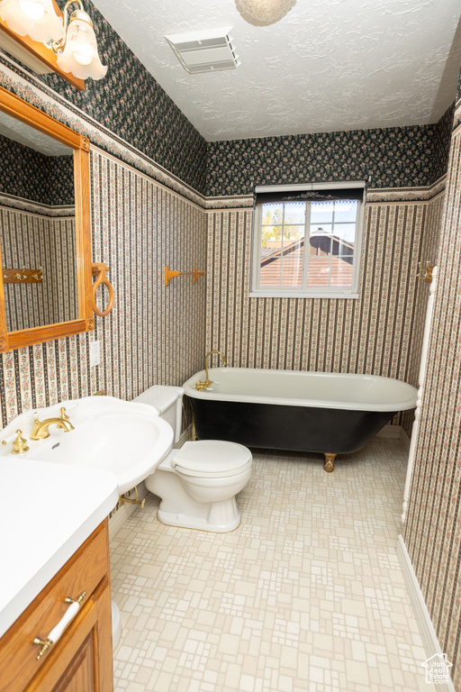 Bathroom featuring toilet, a tub to relax in, vanity, and a textured ceiling