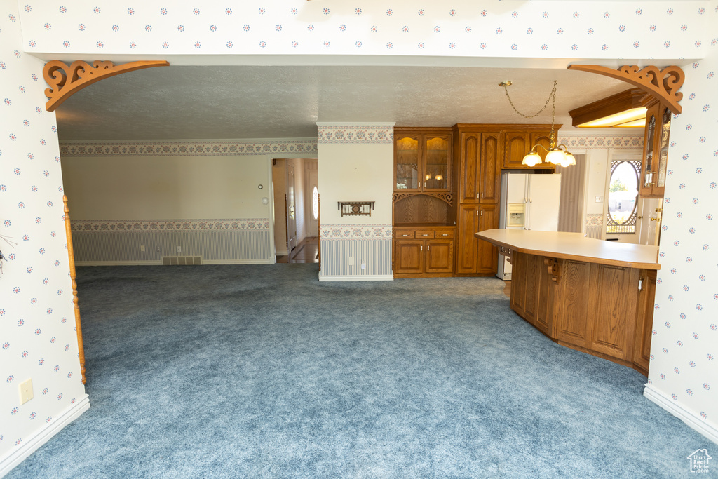 Kitchen with a textured ceiling, dark colored carpet, a notable chandelier, decorative light fixtures, and white refrigerator with ice dispenser