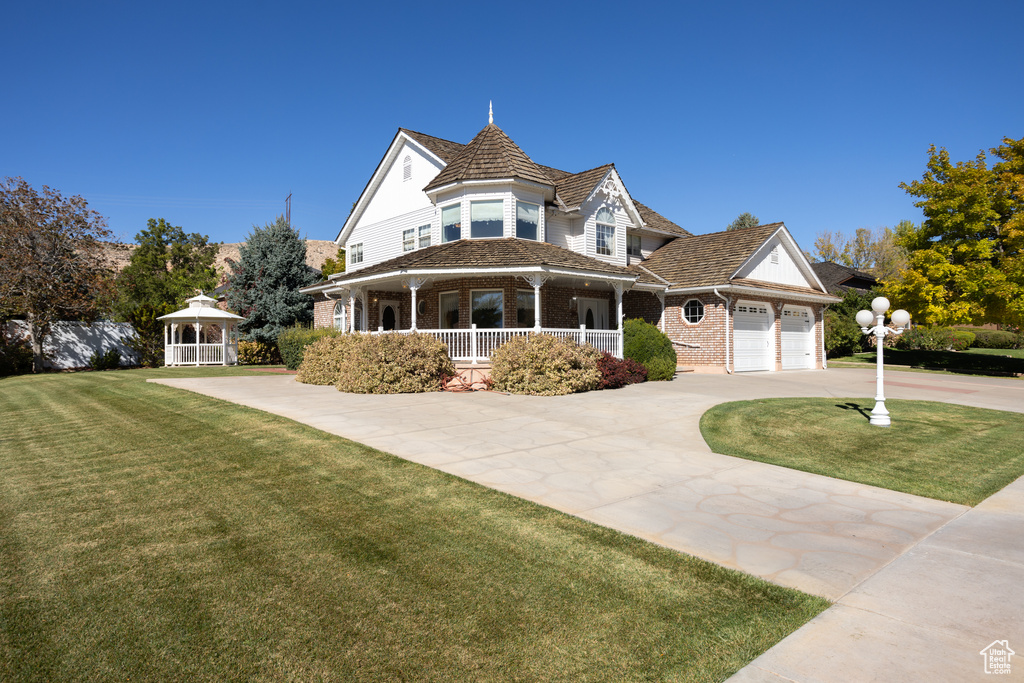 Victorian house featuring covered porch, a gazebo, a front yard, and a garage