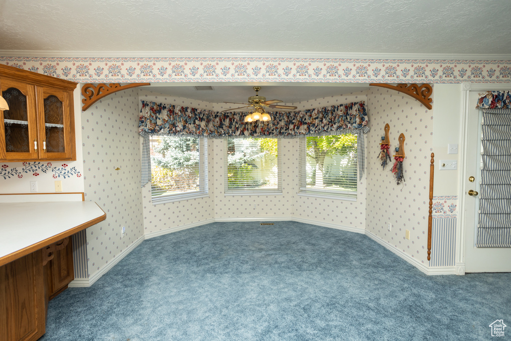 Carpeted dining area with ceiling fan, ornamental molding, and a textured ceiling