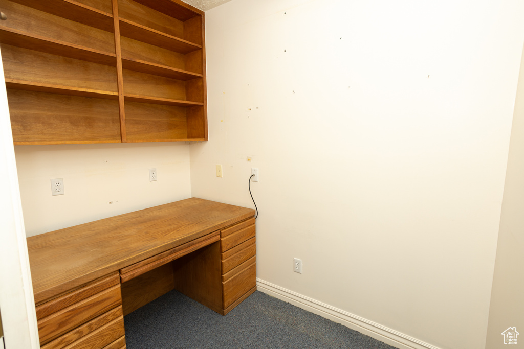 Unfurnished office with built in desk and dark carpet