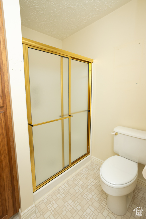 Bathroom featuring a shower with door, a textured ceiling, and toilet