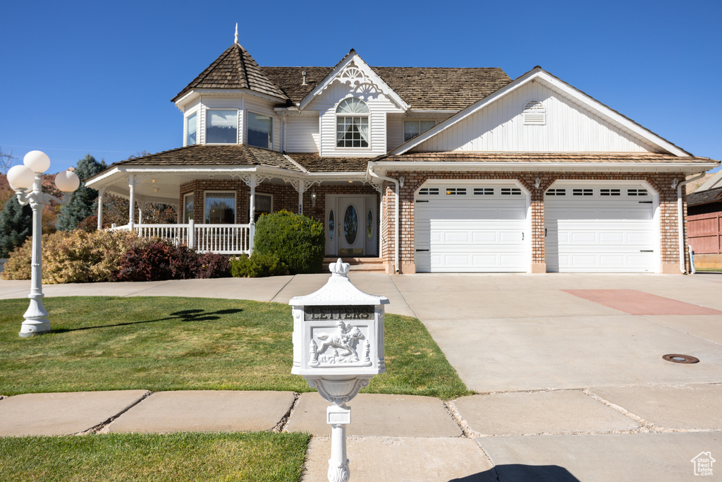 View of front of property with covered porch, a front lawn, and a garage