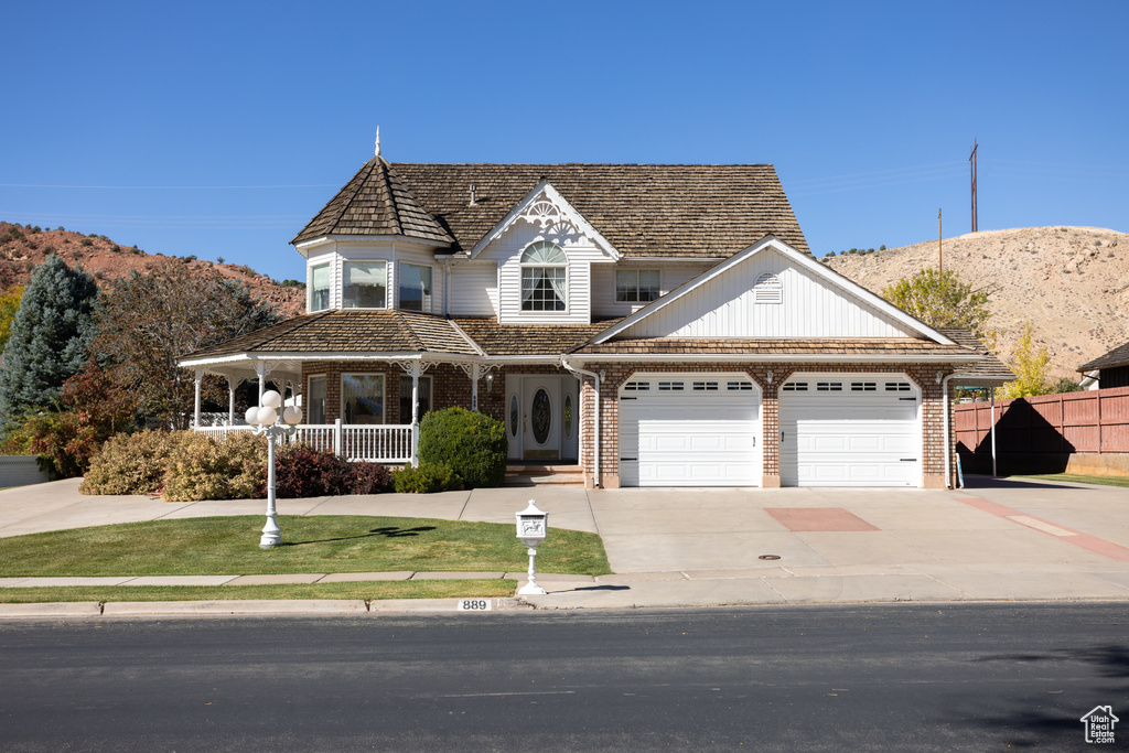 View of front of house featuring a mountain view, covered porch, a garage, and a front lawn