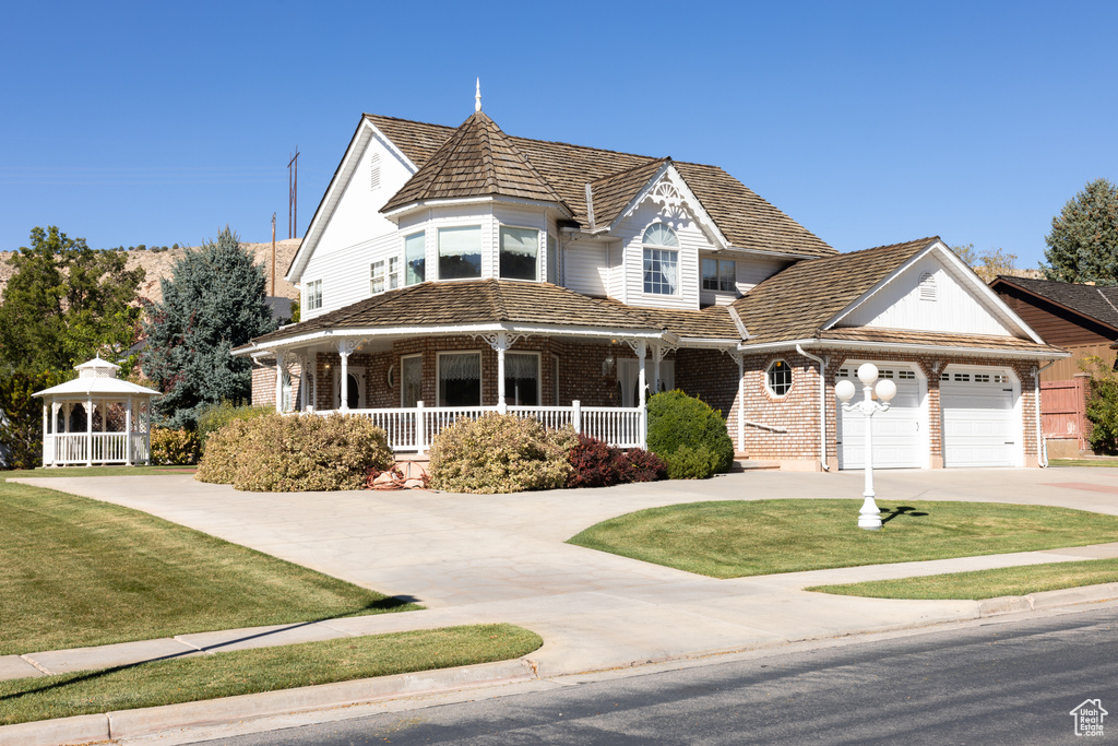 Victorian home with covered porch, a front yard, and a garage